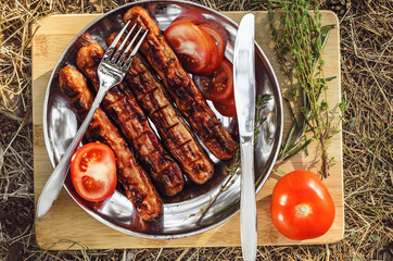 Sausages cooking on grill served on a plate with spices, herbs and tomatoes. Food background with barbecue party, top view