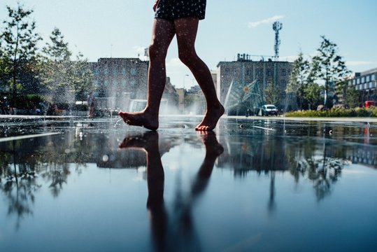 Reflection Of A Barefoot Person On The Wet Sidewalk With Water Fountains