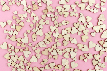 Celebtate greeting card with many small wooden hearts on pink paper surface. Love concept. Top view and flat lay.