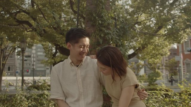 Cheerful Asian Japanese Korean lovers smiling and talking to each other as a sign of successful, happy and contented couple relationship at an outdoor location