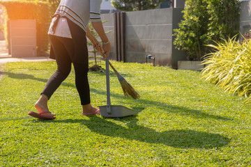 A women sweeping lawns at home in morning with sunlight background