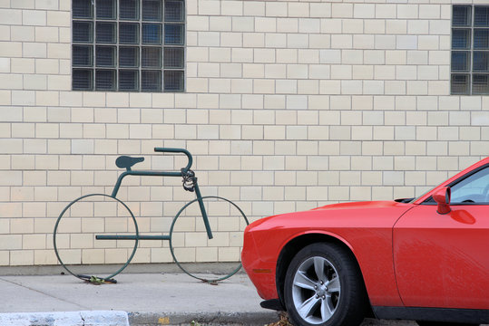 Minimalist contemporary photograph of a car and abstract bike against a brick wall with block-glass windows.