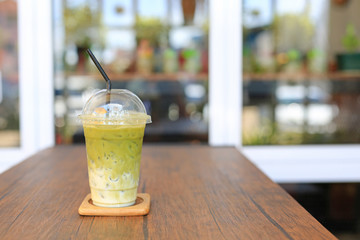 Iced matcha green tea latte with milk with brown straw in take away cup on wooden table at cafe.