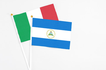 Nicaragua and Italy stick flags on white background. High quality fabric, miniature national flag. Peaceful global concept.White floor for copy space.