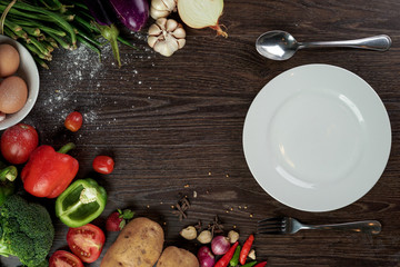 Fresh organic vegetables and seasoning ingredients for tasty vegetarian cooking around blank white plate , top view. Healthy or diet food concept.
