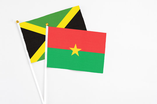 Burkina Faso and Jamaica stick flags on white background. High quality fabric, miniature national flag. Peaceful global concept.White floor for copy space.