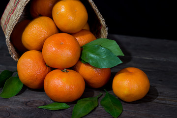 Bright orange tangerines with green leaves in a wicker basket on a dark wooden table. The concept of a healthy diet and vegetarianism.