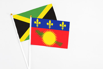 Guadeloupe and Jamaica stick flags on white background. High quality fabric, miniature national flag. Peaceful global concept.White floor for copy space.