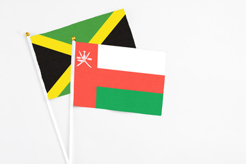 Oman and Jamaica stick flags on white background. High quality fabric, miniature national flag. Peaceful global concept.White floor for copy space.