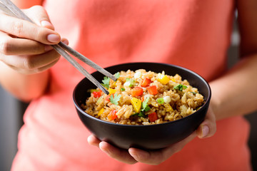 Hand holding chopsticks for eating fried rice with vegetables, Asian food