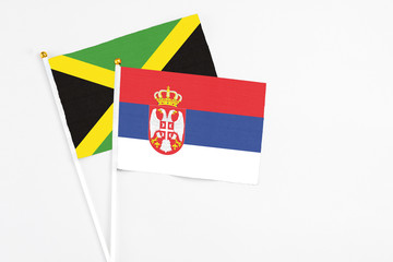 Serbia and Jamaica stick flags on white background. High quality fabric, miniature national flag. Peaceful global concept.White floor for copy space.