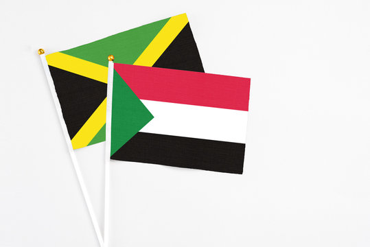 Sudan and Jamaica stick flags on white background. High quality fabric, miniature national flag. Peaceful global concept.White floor for copy space.