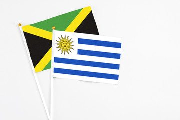 Uruguay and Jamaica stick flags on white background. High quality fabric, miniature national flag. Peaceful global concept.White floor for copy space.
