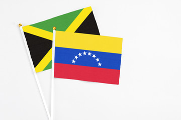 Venezuela and Jamaica stick flags on white background. High quality fabric, miniature national flag. Peaceful global concept.White floor for copy space.