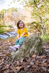 young girl with yellow shirt and green pants sitting on rock
