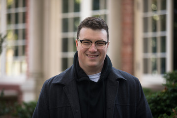 Fototapeta premium A caucasian male wearing a black hoodie sweater and glasses poses in a garden while surrounded by fall foliage on a cold afternoon.