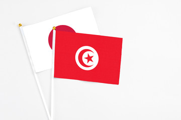 Tunisia and Japan stick flags on white background. High quality fabric, miniature national flag. Peaceful global concept.White floor for copy space.