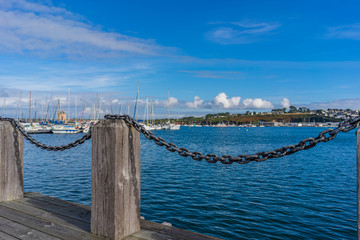 A jetty in a harbor with sailboats in the background which are slightly blurred - 302830724