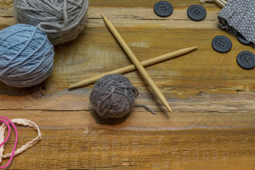 Many different kinds of wool with knitting needles and other accessories lie on an old wooden board - 302830766