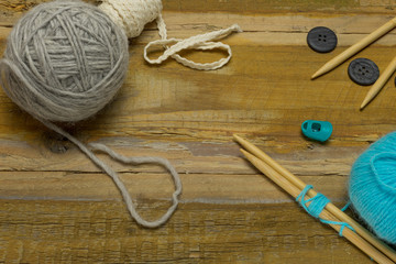 Many different kinds of wool with knitting needles and other accessories lie on an old wooden board - 302830770