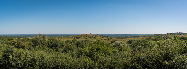 Panorama. Beautiful rural landscape with green hills and trees on a blue sky background