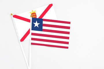 Fototapeta premium Liberia and Jersey stick flags on white background. High quality fabric, miniature national flag. Peaceful global concept.White floor for copy space.