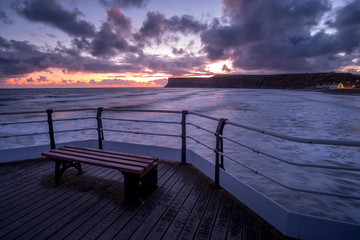 Fototapeta na wymiar Wooden bench on pier overlooking tranquil sunrise at Saltburn by the sea