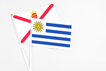 Fototapeta premium Uruguay and Jersey stick flags on white background. High quality fabric, miniature national flag. Peaceful global concept.White floor for copy space.