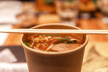 Asian soup in a paper cup with chopsticks. Close-up.