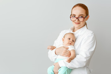 Pediatrician with cute baby on light background