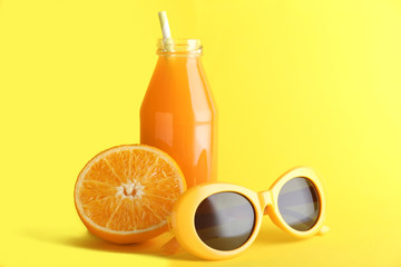 Bottle of fresh orange juice with sunglasses on color background