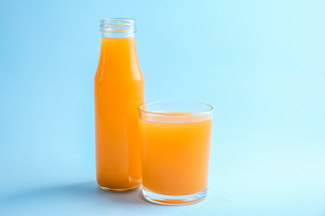 Glass and bottle of fresh orange juice on color background
