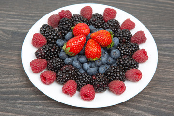 Blackberry, raspberry blueberry and strawberry on a white plate. Vitamins and wholesome foods