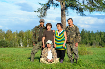 Obraz premium Two Yakut Asian elderly couples men and women with a young girl sitting on the grass pose for a family photo in a field near a tree.