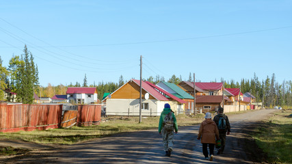 Yakut family of men with a woman and one young girl with a backpack is on the road in the new area of private houses in the village of Suntar in Yakutia.