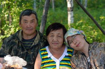 Family portrait of two elderly and one young daughter Yakut Asians in the Northern forest at the table.
