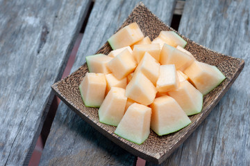 Sliced Cantaloupe in wooden plate on old table background.