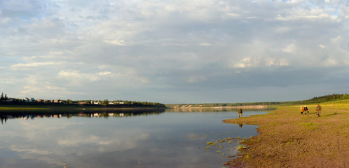 Two elderly men and two Yakut women talking walk along the Bank of the Northern Viluy river at sunset against the background of the houses of the village of Suntar on the other Bank.