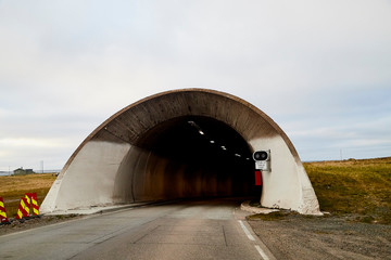 The entrance to the tunnel in Norway. Grey track going in the tunnel and sky with clouds under it