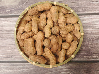 Top view of a pile of raw peanuts also called groundnut on bamboo plate isolated on wooden background. Food concept. With edible seeds and high oil content. Oil crop. Common ingredients in Taiwan.