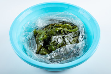 Fresh green salted sea cabbage stems in a pot on white background