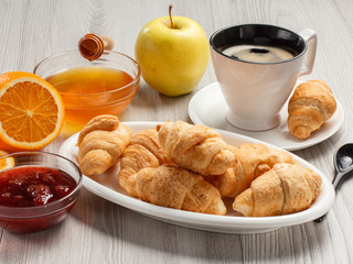 Cup of black coffee with saucer, fresh croissants on white porcelain dish