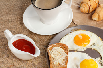 Plate with fried eggs and toast with butter, croissants and cup of coffee.
