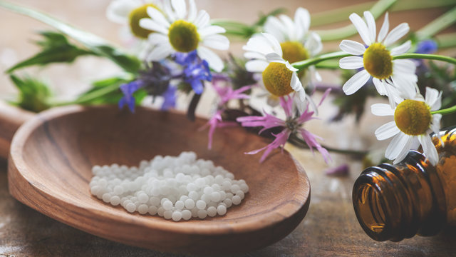 Hom&ouml;opathie-Globuli auf einem Holzl&ouml;ffel mit Fl&auml;schchen und Heilpflanzen