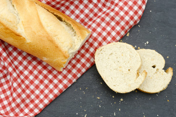 rustic crusty white bread lying on black slate on red white towel in the kitchen