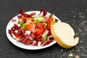 mixed salad and rustic crusty white bread lying on black slate in the kitchen