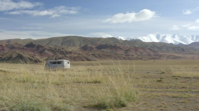 Aerial, tracking, drone shot, of a van, driving on a desert road, on a field, in the Altai mountains, on a partly sunny day, near Bayan-Olgii, in Mongolia