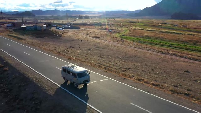 Aerial, orbit, drone shot, around a van, driving on a road, at a desert, in the Altai mountains, on a cloudy day, near Bayan-Olgii, in Mongolia