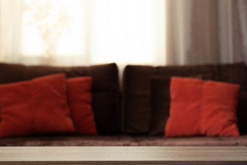 Empty wooden table for products against defocused sofa with pillows. Front view. Soft focus. Template