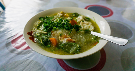 The close up view of the mixed vegetables soup with soo hoon noodles in a bowl.